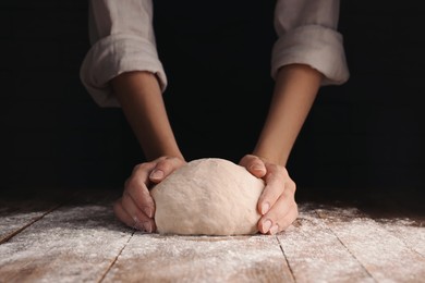 Photo of Woman kneading dough at table on dark background, closeup