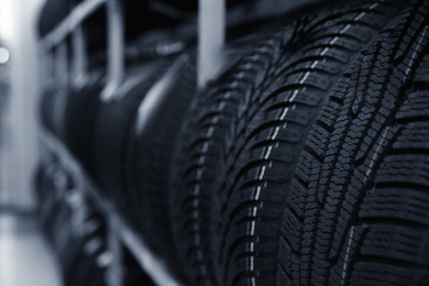 Car tires on rack in auto store, closeup. Space for text