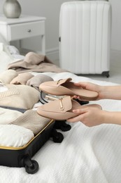 Photo of Woman holding fashionable shoes near open suitcase in bedroom, closeup