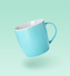 Image of One empty ceramic cup falling on light turquoise background