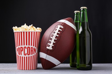 American football ball with popcorn and beer on grey wooden table