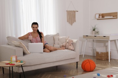 Happy young mother with cup of coffee and laptop resting in messy living room
