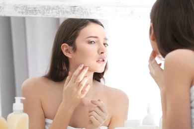 Teenage girl with acne problem looking in mirror indoors