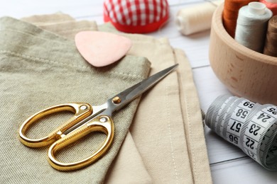 Photo of Scissors, spools of threads and sewing tools on white wooden table, closeup
