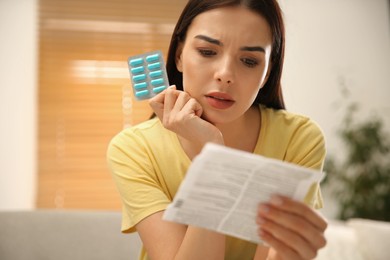 Photo of Confused young woman with pills reading medicine instruction at home