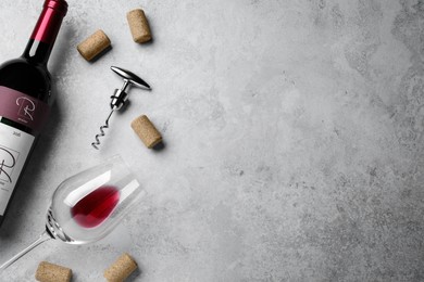 Corkscrew with wine bottle, glass and stoppers on light grey stone table, flat lay. Space for text