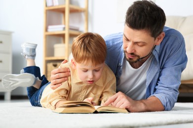 Photo of Father reading book with his son on floor in living room at home
