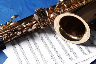 Beautiful saxophone and note sheets on blue wooden background, closeup