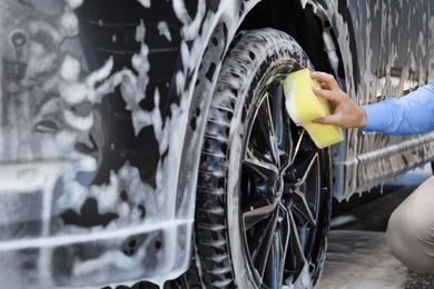 Businessman cleaning auto with sponge at self-service car wash, closeup