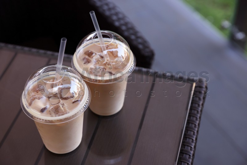 Plastic takeaway cups of delicious iced coffee on table in outdoor cafe, space for text