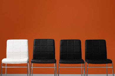 Photo of Black chairs with white one near orange wall, space for text. Recruiter searching employee