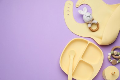 Set of plastic dishware, silicone bib and baby accessories on violet background, flat lay. Space for text