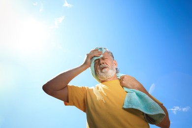 Senior man with towel suffering from heat stroke outdoors, low angle view