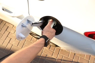 Man inserting plug into electric car socket at charging station, above view