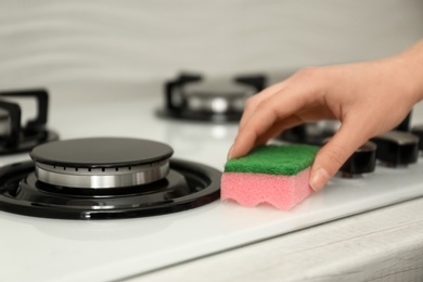 Photo of Woman cleaning gas stove with sponge, closeup