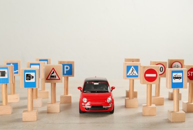 Many different miniature road signs and car on wooden table, space for text. Driving school