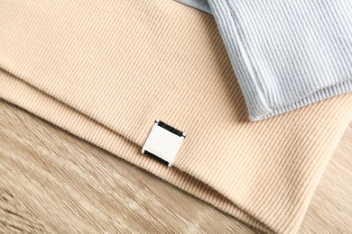 Beige apparel with blank clothing label on wooden table, top view