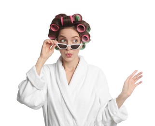 Emotional young woman in bathrobe with hair curlers and sunglasses on white background