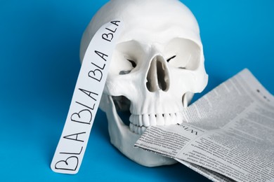 Photo of Information warfare concept. Useless nonsense in mind as result of media propaganda influence. Human skull with newspaper on light blue background, closeup