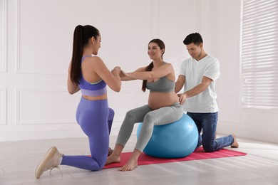 Pregnant woman and her husband working with trainer in gym. Preparation for child birth