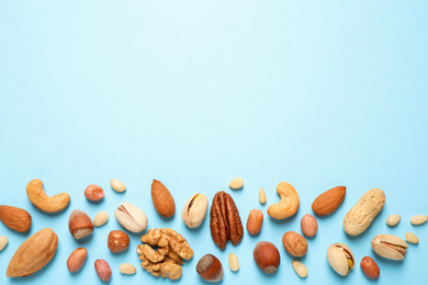 Photo of Different delicious nuts on light blue background, flat lay. Space for text