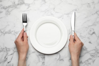 Woman with empty plate and cutlery at white marble table, top view