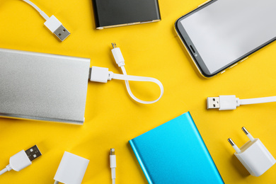 Mobile phone and portable chargers on yellow background, flat lay