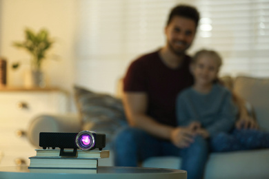 Young man and her daughter watching movie at home, focus on video projector