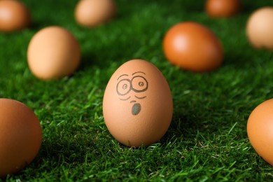 Photo of Egg with drawn surprised face among others on green grass