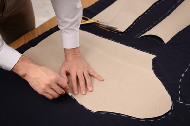 Tailor marking sewing pattern on fabric with chalk at table, closeup