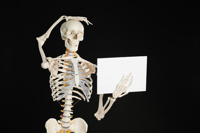 Artificial human skeleton model with blank paper sheet on black background. Space for text