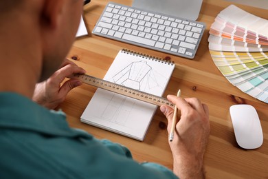 Man with sketchbook, pencil and ruler at wooden table, closeup
