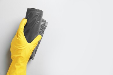 Janitor in rubber glove holding roll of grey garbage bags over light background, top view. Space for text