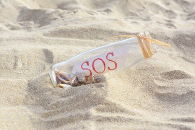 Glass bottle with seashells and message SOS on sand