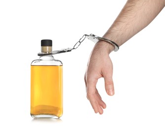 Addicted man in handcuffs with bottle of alcoholic drink on white background, closeup