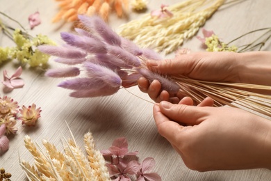 Florist making bouquet of dried flowers at white wooden table, closeup