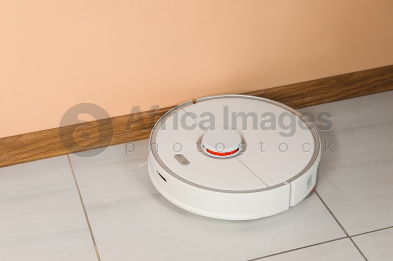 Robotic vacuum cleaner on white tiled floor near beige wall