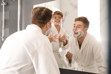 Dad and son with shaving foam on faces in bathroom