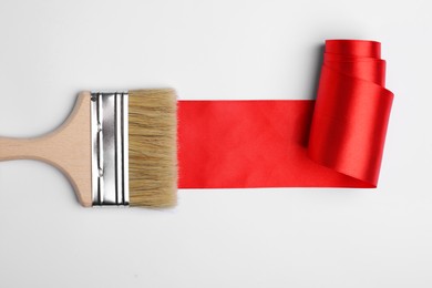 Brush painting with red ribbon on light background, top view. Creative concept