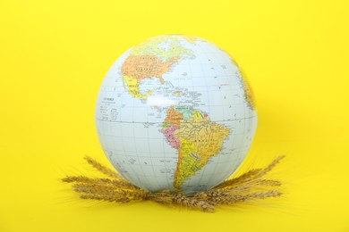 Photo of Globe with wheat spikelets on yellow background. Hunger crisis concept