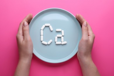 Woman holding plate with calcium symbol made of white pills on bright pink background, top view