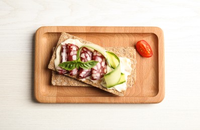 Photo of Fresh rye crispbreads with salami, cream cheese and cucumber on white wooden table, top view