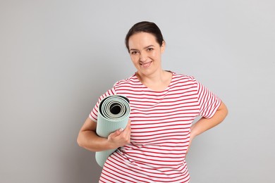 Happy overweight woman with yoga mat on grey background