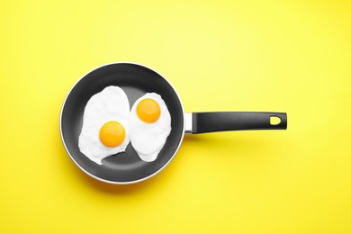 Tasty fried eggs in pan on yellow background, top view