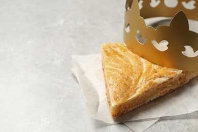 Slice of traditional galette des Rois with paper crown on light grey table. Space for text