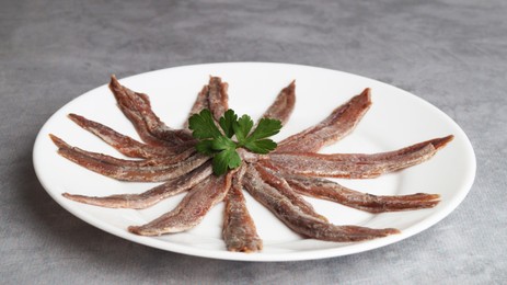 Photo of Plate with anchovy fillets and parsley on grey table, closeup
