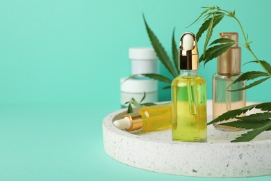 Bottles of hemp cosmetics and green leaves on turquoise background, space for text