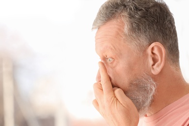 Senior man putting contact lens in his eye on blurred background