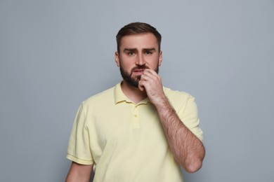 Man biting his nails on grey background. Bad habit