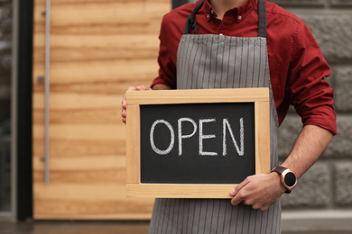 Photo of Young male business owner holding OPEN sign near his cafe, closeup